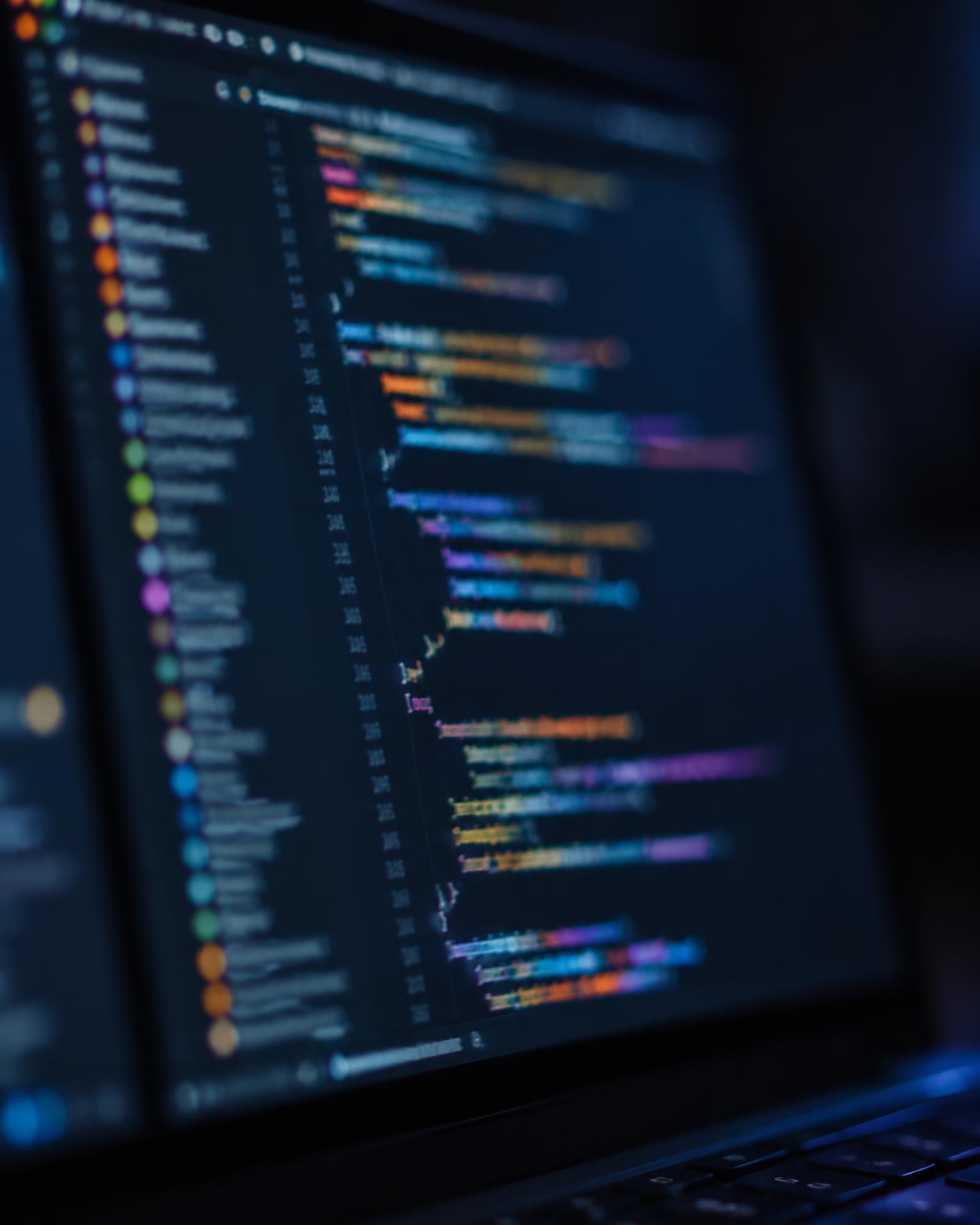 Illustrative macro photograph of a laptop screen showing blurred, colour-highlighted program code